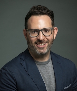 A man in a dark jacket smiles at the camera.