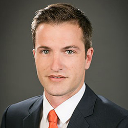 Man in dark grey suit with white shirt and red tie 