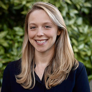 A blond woman in a dark top smiles.