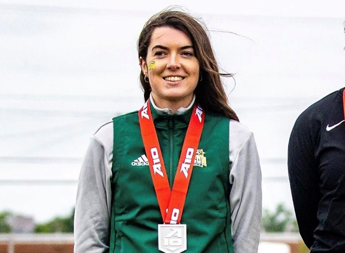 A woman with a Mason face paint badge stands on a podium with a silver medal around her neck.