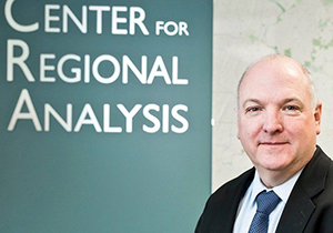 A man in front of a Center for Regional Analysis sign in a suit and tie looks at the camera.
