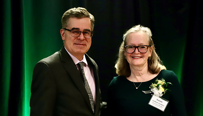 A woman and a man pose in front of a green curtain.