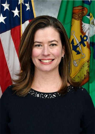 A woman in a dark dress in front of flags smiles at the camera.