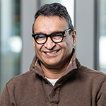 A man in a brown jacket stands and smiles