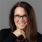 A woman wearing a black shirt and holding her right hand under her chin smiles