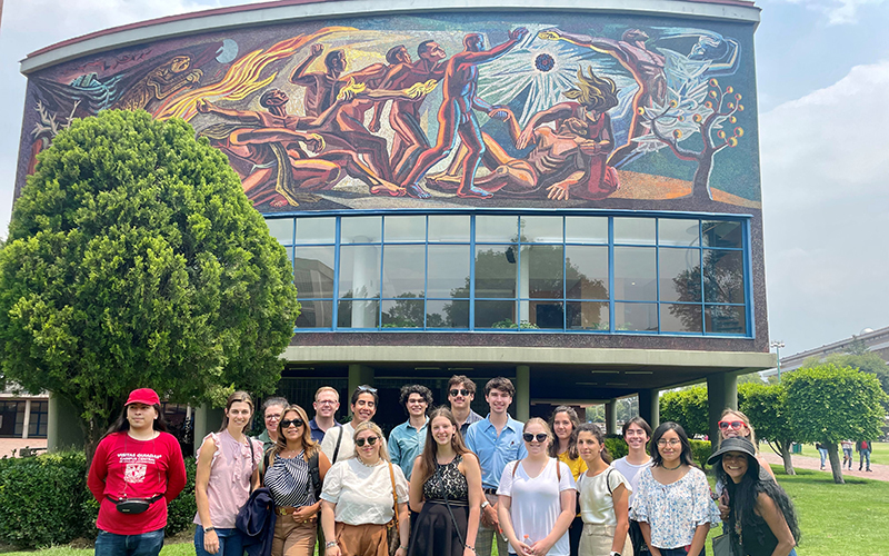 A crowd of people pose in front of a color mural.