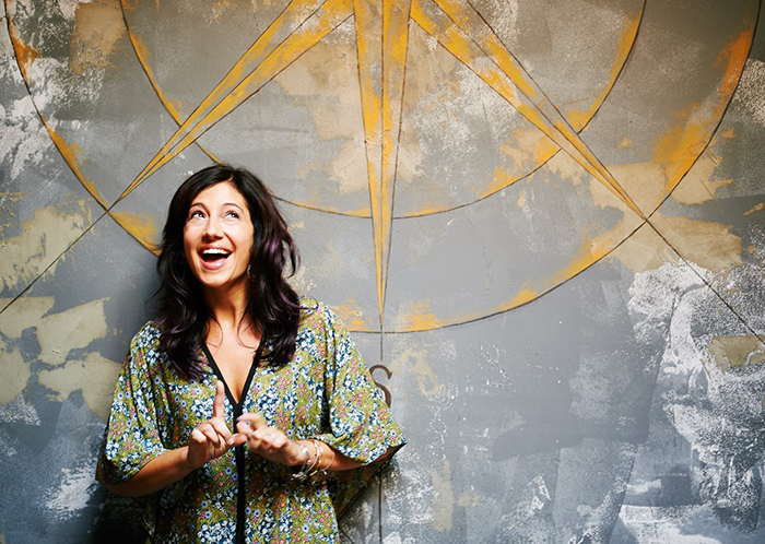 A woman in a floral gown and dark hair looks up as she stands in front of a compass.