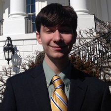 David Glietz, BS Public Administration, wearing a black suit and green collared shirt with a green and gold tie.