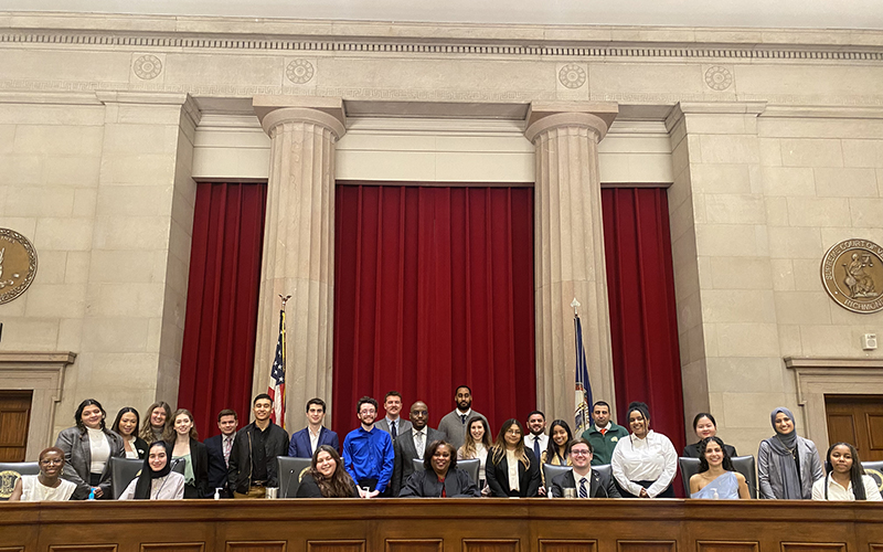 A group of students congregates around the bench and in front of two stone columns at the Supreme Court of Virginia.