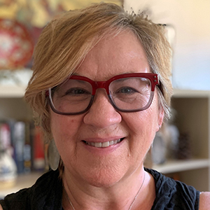 A woman with eyeglasses and a jade pendant on her neck smiles.