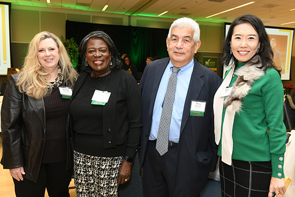 A photo of four individuals standing inside and smiling for the camera.