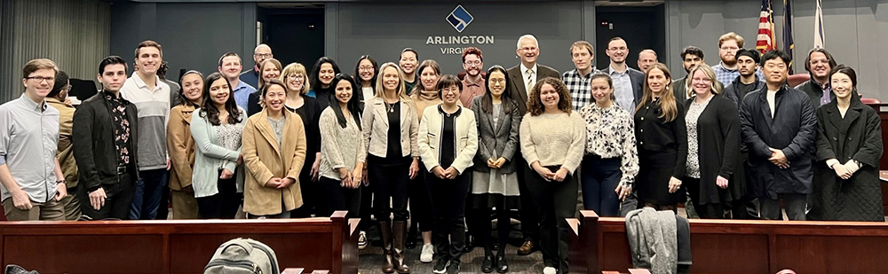 About 30 people and facing the camera in front of a sign reading Arlington County.