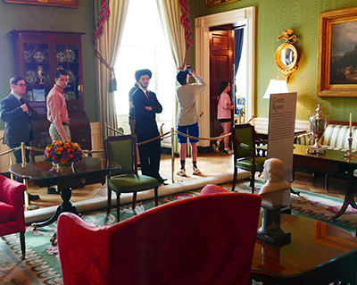 Three young men look at the antique furniture in a formal room.