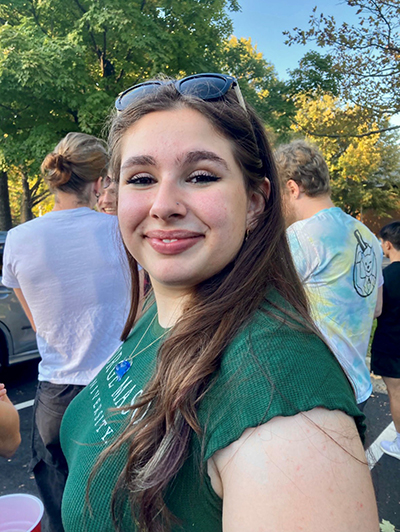 A young woman in a green shirt and with sunglasses atop her head smiles at the camera.