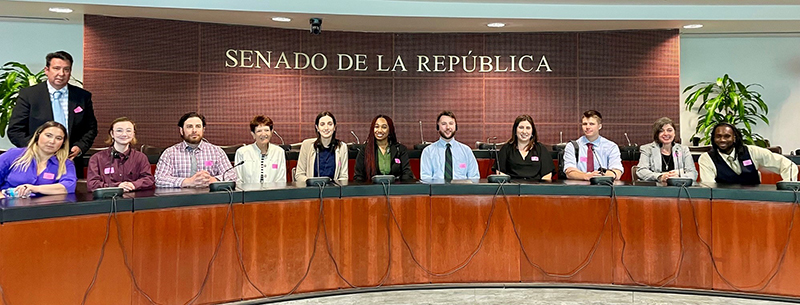 A small group of college students sit behind a large, very formal desk.