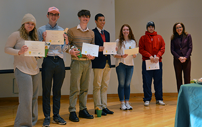 Six students in a line hold certificates at the front of a conference room.