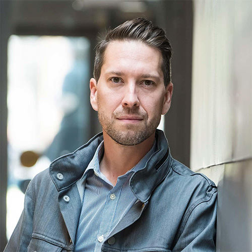 Young man wearing a light gray blazer standing against a building