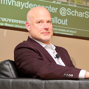 A bald man in a leather chair looks to his right in a closeup.