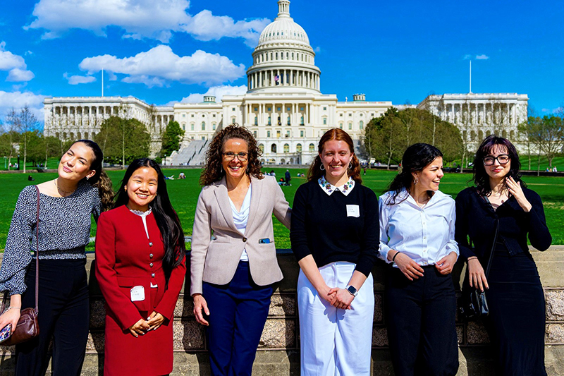 Six women stand in front of the Capitol Building on a sunny day.
