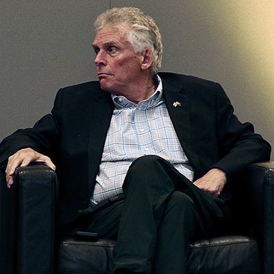 A man in a dark jacket and silver hair looks to his right.