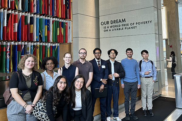 A group of students stand in front of international flags and a pillar saying, ‘Our dream is a world free of poverty on a livable planet.’