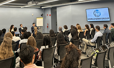 A woman and two men sit in front of a conference room talking to a group of students.
