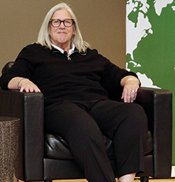A woman with blonde hair in a black outfit looks at the camera.