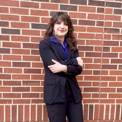 A young woman in black leans against a brick wall.
