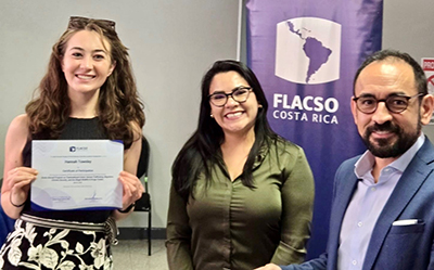 A woman in a black top holds a certificate as a woman and a man next to her smile at the camera.