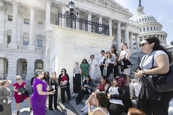 A woman in a purple dress addresses several young women standing on the steps of the U.S. Capitol.