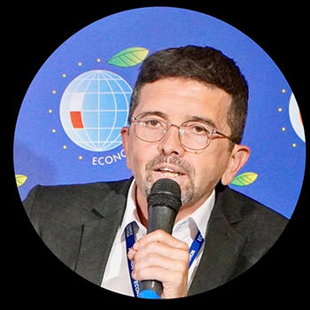 A man with dark hair and eyeglasses holds a microphone.